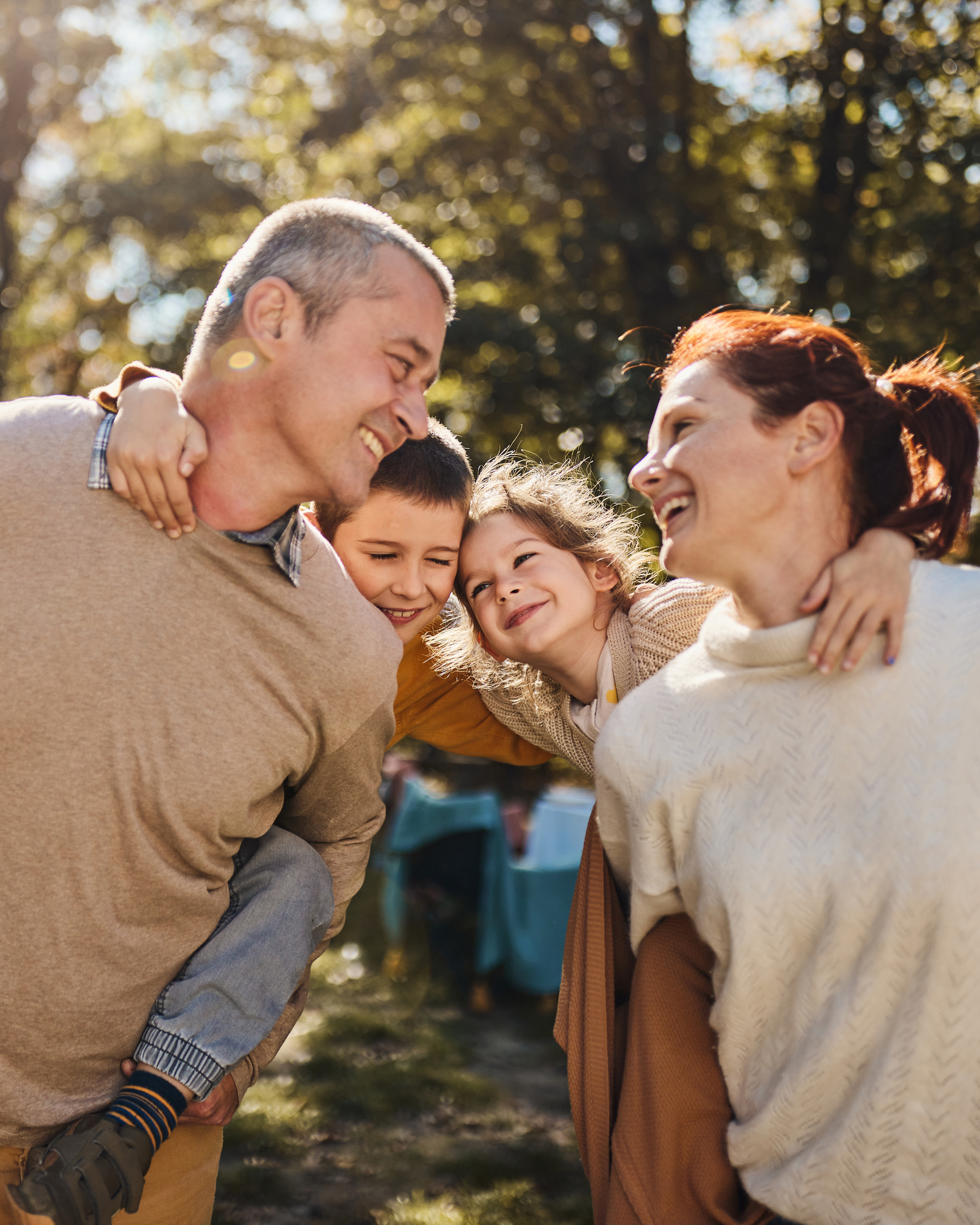 Happy parents having fun while piggybacking their small kids during autumn day in nature.
